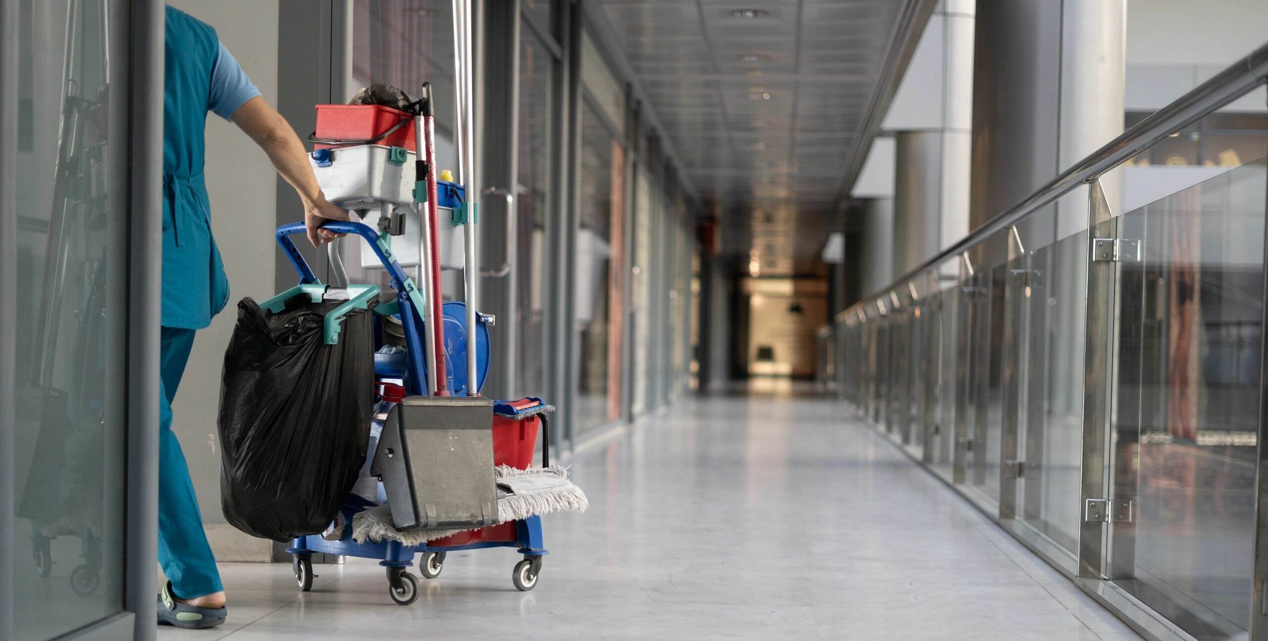 Janitorial cart with cleaning supplies in a long hallway.