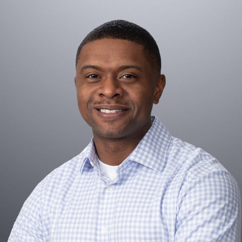 Smiling man in a checkered shirt against a neutral background.