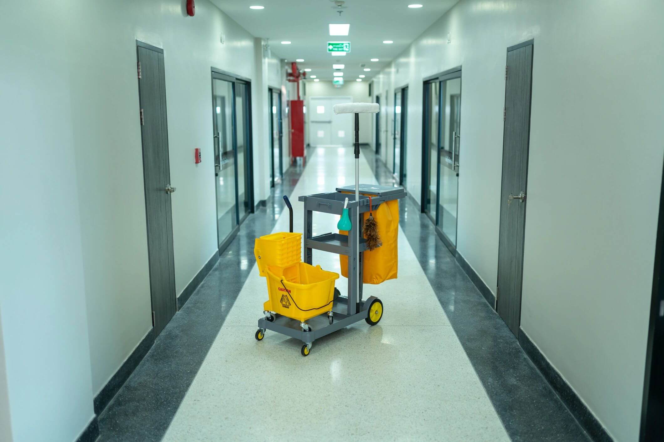 Cleaning cart with mop and bucket in a hallway.
