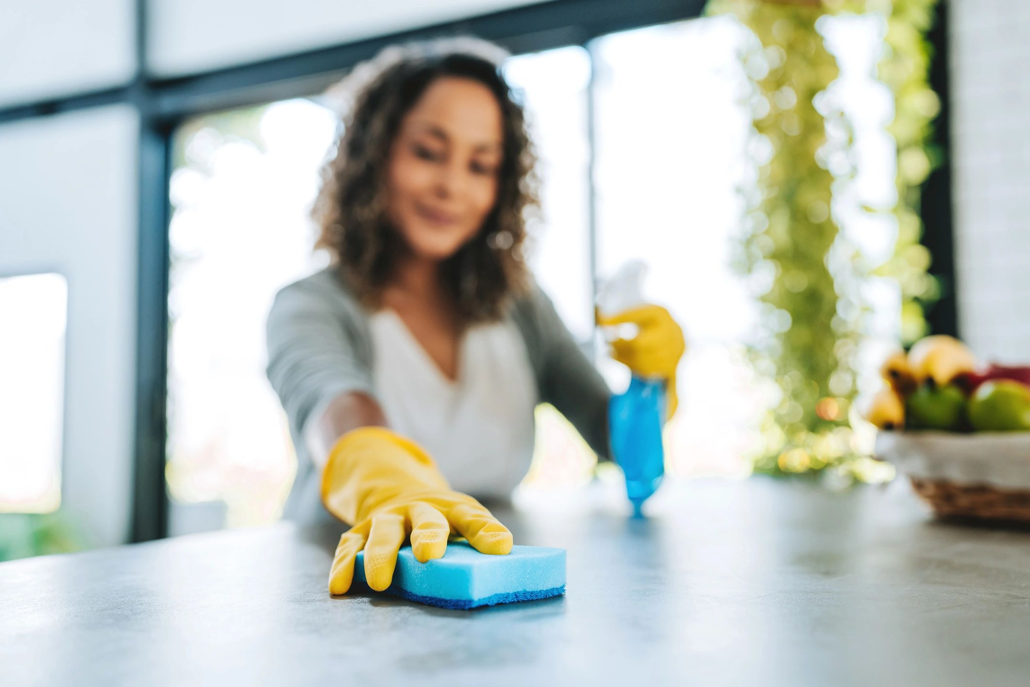 Woman cleaning a surface with a sponge and spray bottle.