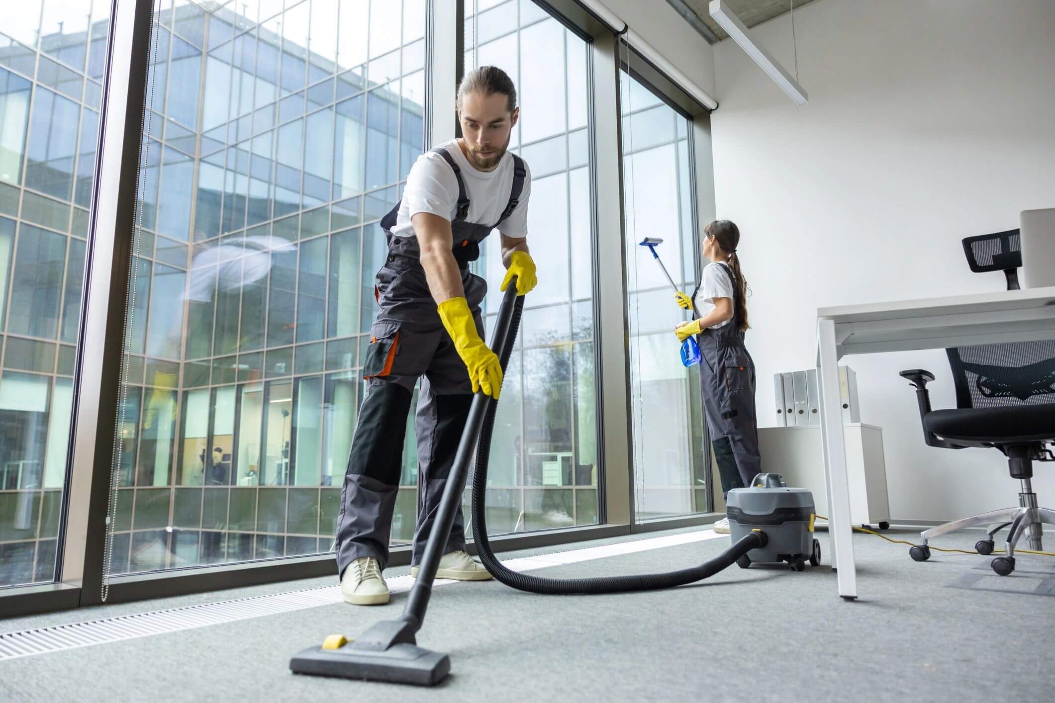 Two janitors cleaning a modern office with vacuum and mop.