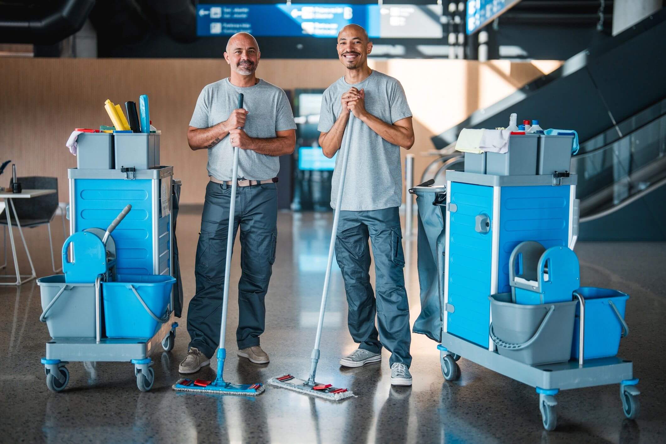 Two janitors smiling with mops in a clean, well-lit facility.
