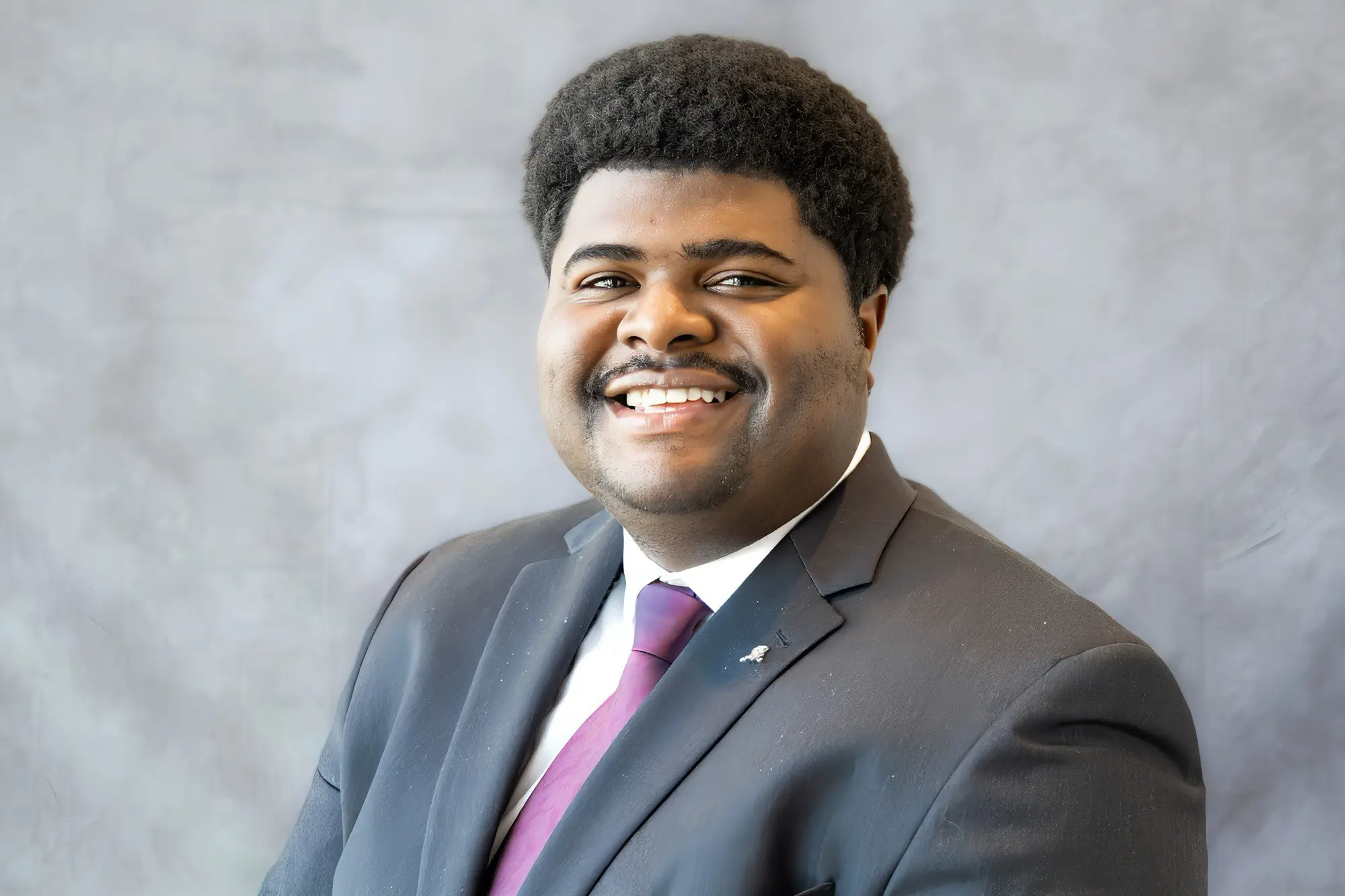 Smiling man in a suit and tie with a gray background.